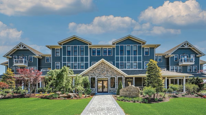 A large, modern building with a stone facade and glass windows, surrounded by landscaped gardens under a partly cloudy sky.