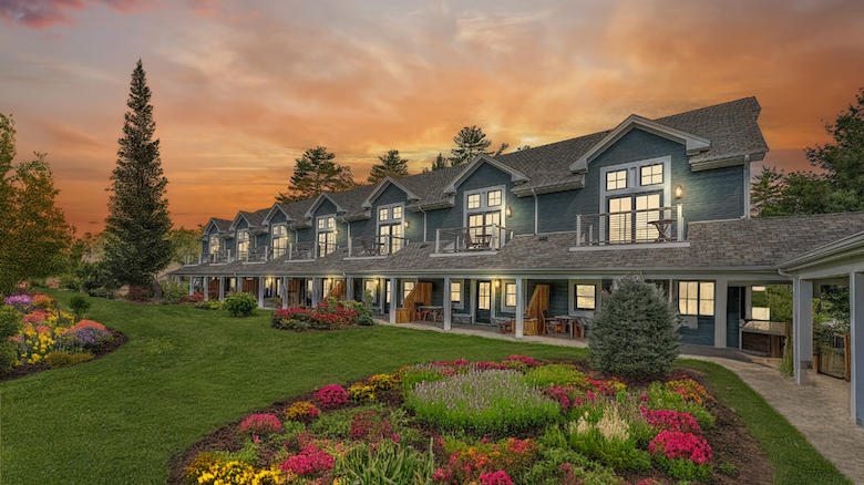 A row of cozy houses with balconies, set against a sunset sky. Beautifully landscaped gardens and lush greenery surround the scene.