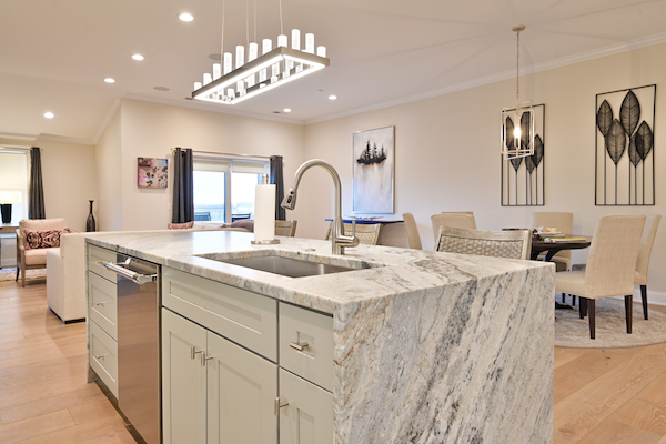 The image shows a modern kitchen with a marble island, stainless steel appliances, and a dining area with a table and chairs in the background.