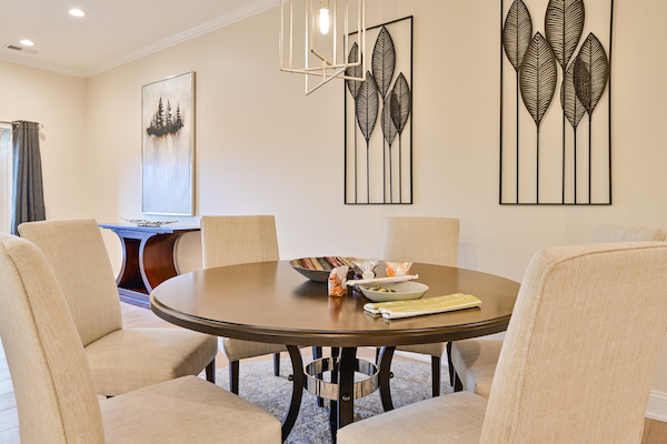 A modern dining room features a round table with six chairs, a decorative centerpiece, and framed artwork on the beige walls.