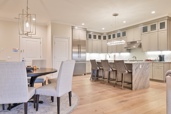 A modern kitchen and dining area with light wood flooring, marble countertops, beige cabinetry, a round dining table with four chairs, and a kitchen island.