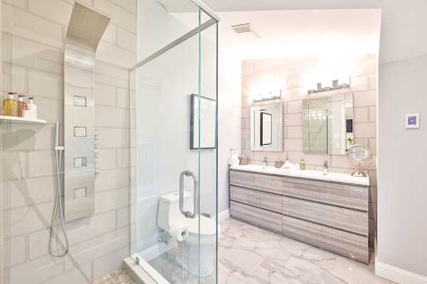 A modern bathroom with a glass shower enclosure, wall-mounted showerhead, and a double-sink vanity with a large mirror above it.