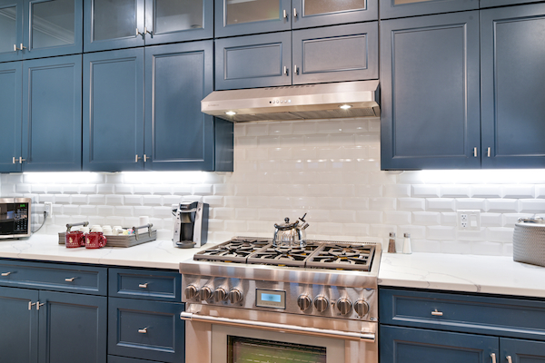 A modern kitchen with blue cabinets, a stainless steel stove and hood, white subway tiles, and a countertop coffee maker and toaster.