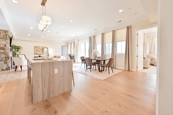 An open-concept kitchen and dining area with bright natural light, modern furniture, hardwood floors, and a spacious layout leading to another room.