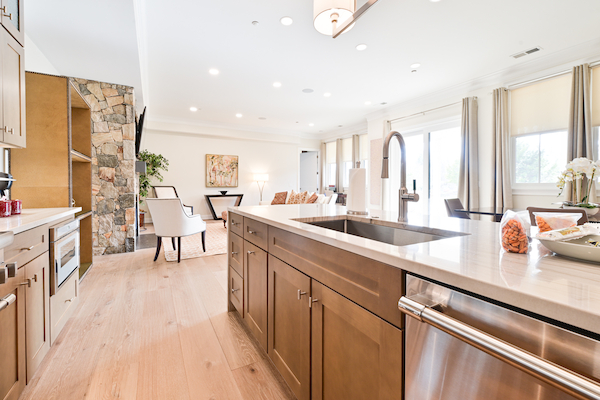 A modern open-concept kitchen with wooden cabinets, a large island, and a view into a living area with a stone wall and large windows ending the sentence.