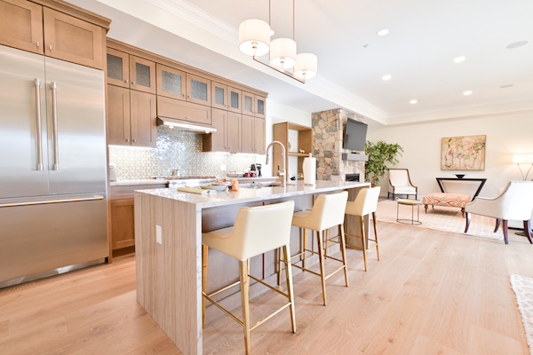 A modern kitchen with light wood cabinetry, a large island with barstools, stainless steel appliances, and a stylish sitting area.