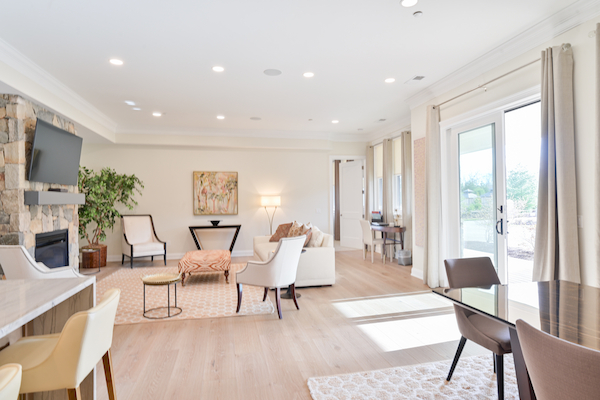 Bright and modern living room with light wooden flooring, comfortable seating, a wall-mounted TV, and large windows bringing in natural light.