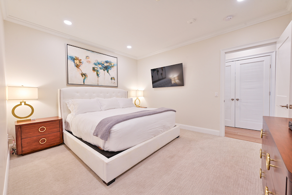 A modern bedroom with a large bed, two bedside tables with lamps, a wall-mounted TV, and abstract artwork above the bed ends the sentence.