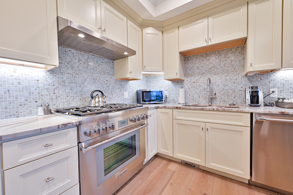 A modern kitchen with white cabinets, stainless steel appliances, a gas stove, oven, dishwasher, and a tiled backsplash, brightly lit, ending the sentence.