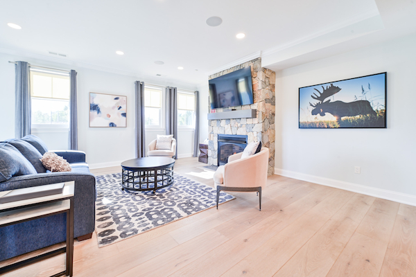 This image shows a modern living room with a blue sofa, beige chairs, a round coffee table, a stone fireplace, wall art, and a mounted TV.