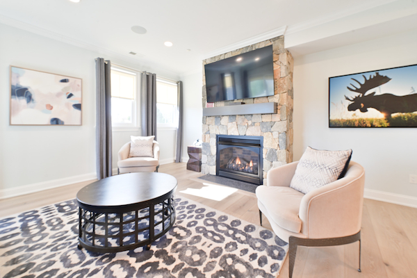 A modern living room with a fireplace, TV, armchairs, a black table, and abstract art on light-colored walls, with a rug and large windows ending the sentence.