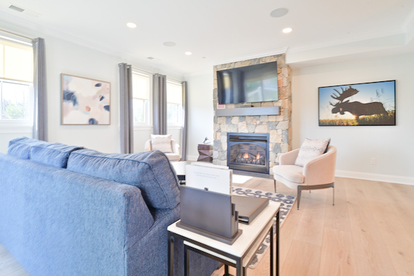 A modern living room with a blue sofa, stone fireplace, wall-mounted TV, abstract paintings, and large windows with gray curtains ending the sentence.