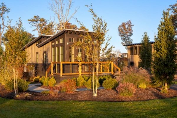 A modern house with large windows, surrounded by lush landscaping, situated in a serene environment with trees and a vibrant green lawn ending the sentence.