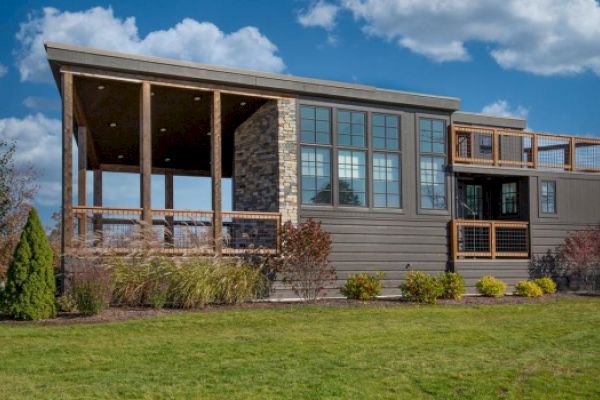 A modern two-story house with large windows, wooden accents, a spacious porch, and a well-maintained lawn under a partly cloudy sky ending the sentence.