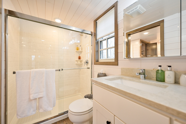 This image shows a clean, modern bathroom with a glass-enclosed shower, white vanity, large mirror, and neatly arranged toiletries.