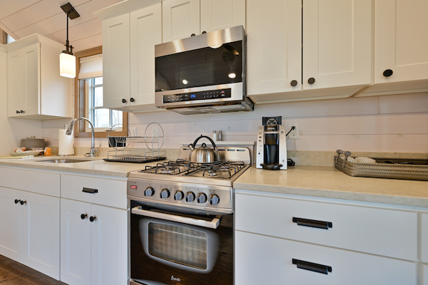 A modern kitchen with white cabinets, a stainless steel oven, microwave, and coffee maker on the counter ending the sentence.