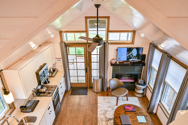 A cozy and modern tiny house interior featuring a kitchen, a living area with a fireplace and TV, and a ceiling fan.