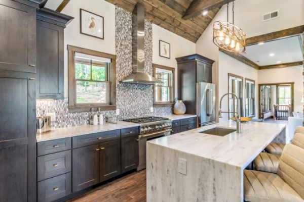 A modern kitchen features dark cabinets, a marble island with barstools, stainless steel appliances, and a decorative backsplash, ending the sentence.