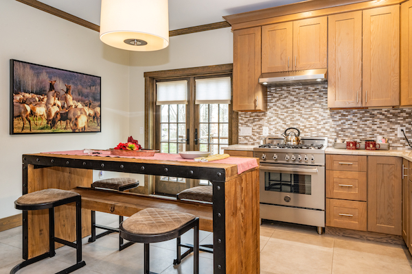 A modern kitchen with wooden cabinets, a center island with seating, a stove, and a window; a painting of deer on the wall.