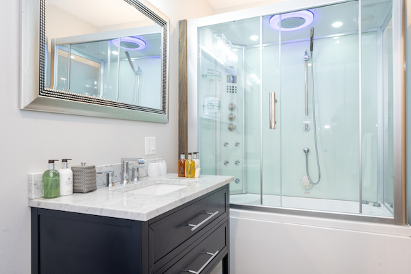 A modern bathroom featuring a glass-enclosed shower with a sleek design, a vanity with a marble countertop, and a large mirror above it.