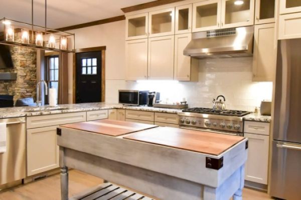 This image shows a modern kitchen with white cabinets, stainless steel appliances, and a large wooden island in the center, ending the sentence.