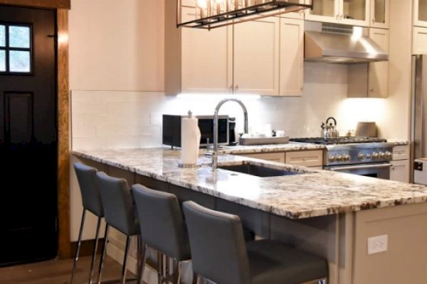 A modern kitchen with white cabinetry, granite countertops, a stainless steel stove, and fridge, with four barstools at the kitchen island.