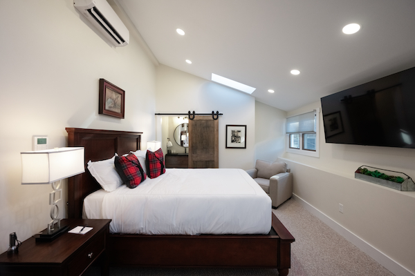 A modern bedroom features a large bed with plaid pillows, a flat-screen TV, a cozy armchair, and sliding barn doors.