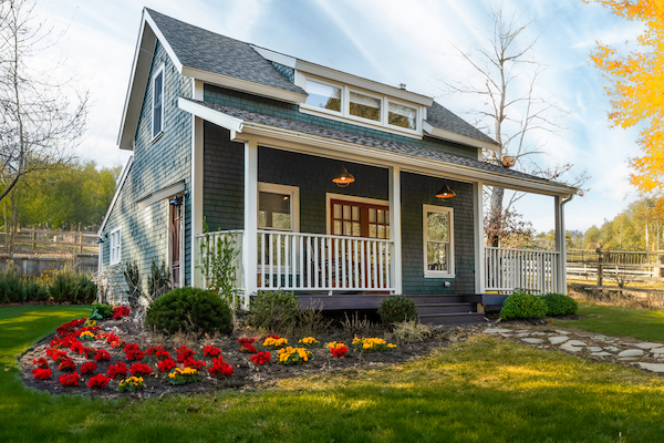 A charming house with a porch, surrounded by a well-maintained garden with colorful flowers, set against a backdrop of greenery and clear skies.