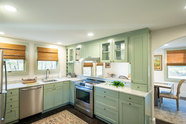 This image shows a modern kitchen with mint green cabinets, stainless steel appliances, a rug, and a view of a dining area.