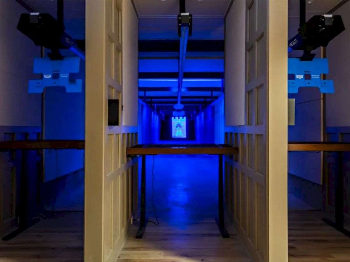 The image shows a corridor illuminated by blue lights, with equipment mounted on the walls and ceiling. A distant image is visible at the end.