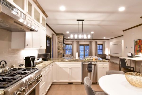 Modern kitchen with white cabinetry, stainless steel appliances, stone backsplash, and an island with seating. Comfy living area visible.