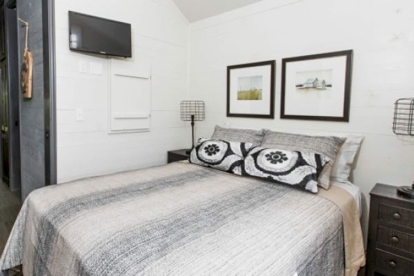 A cozy bedroom with a bed, two nightstands, wall-mounted TV, and framed artwork above the bed. Decor is minimalistic and modern.