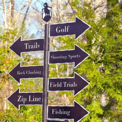 A signpost with directional arrows points to various recreational activities: Golf, Trails, Shooting Sports, Rock Climbing, Field Trials, Zip Line, Fishing.