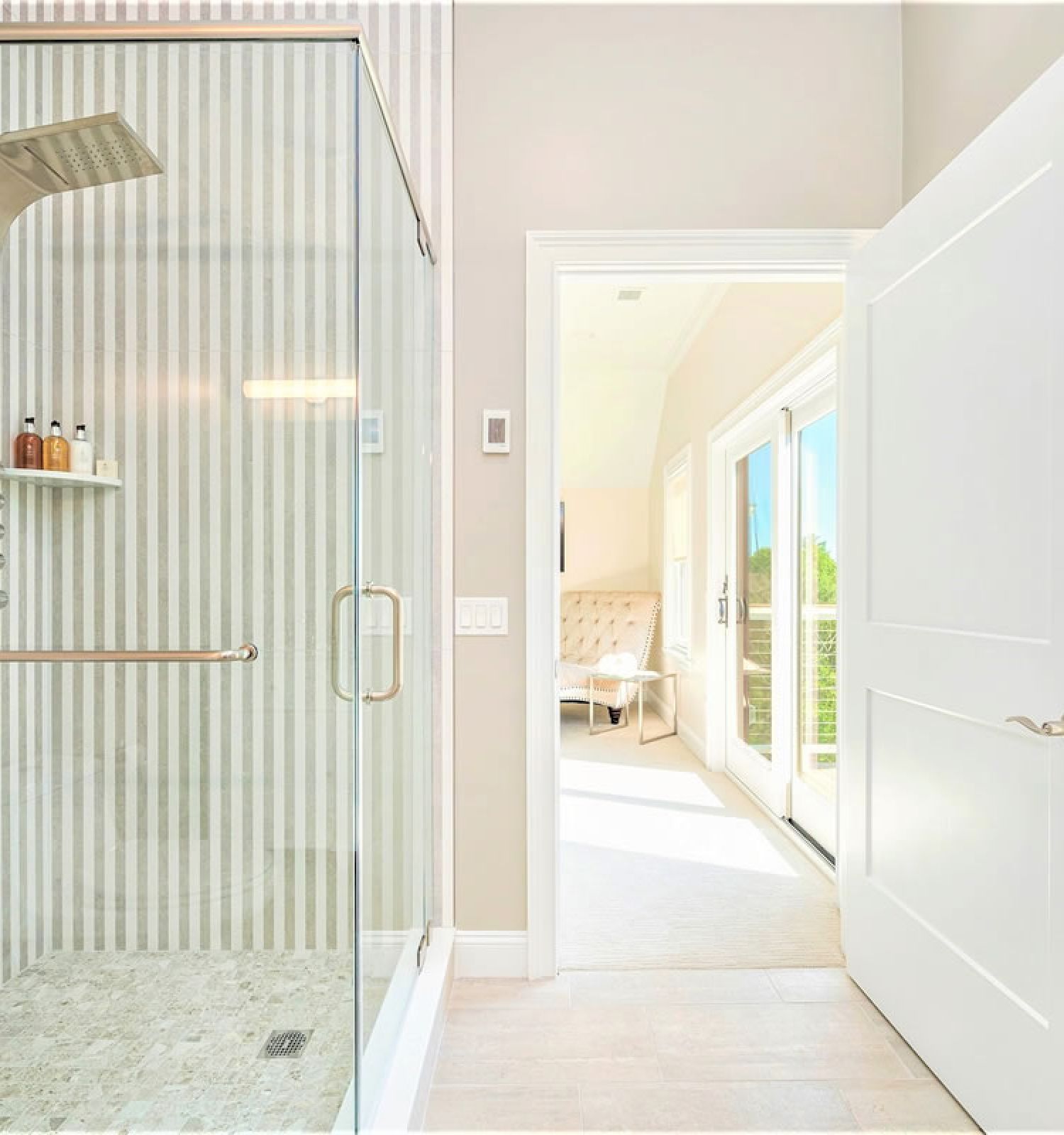 Modern bathroom with striped wall, glass shower enclosure, and open door leading to a brightly lit, white-themed adjacent room.