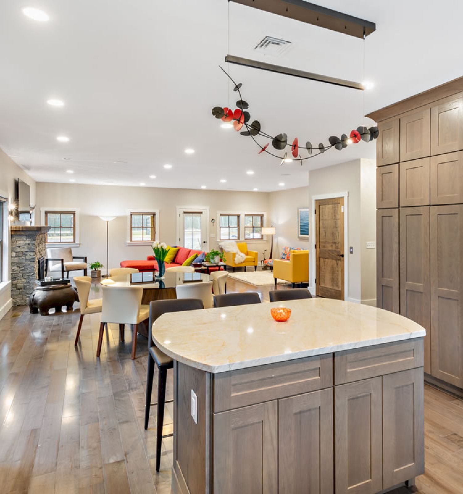 This is an image of an open-concept kitchen and living area with wooden cabinets, a refrigerator, an island, and colorful furniture in the background.