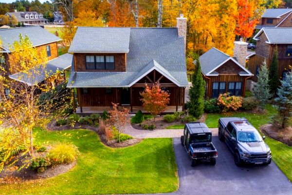 A picturesque house with a well-manicured lawn, fall foliage, and two vehicles parked in the driveway.