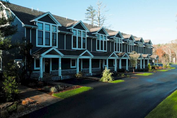 The image shows a row of modern, semi-detached houses along a paved road with neat lawns and trees, under a clear blue sky, ending the sentence.