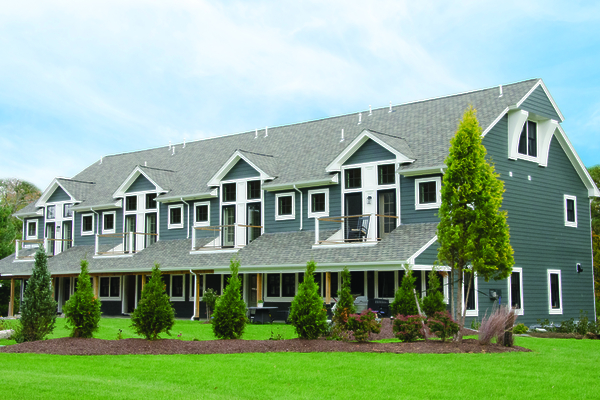 A two-story residential building with multiple windows and balconies, surrounded by a manicured lawn and some trees.