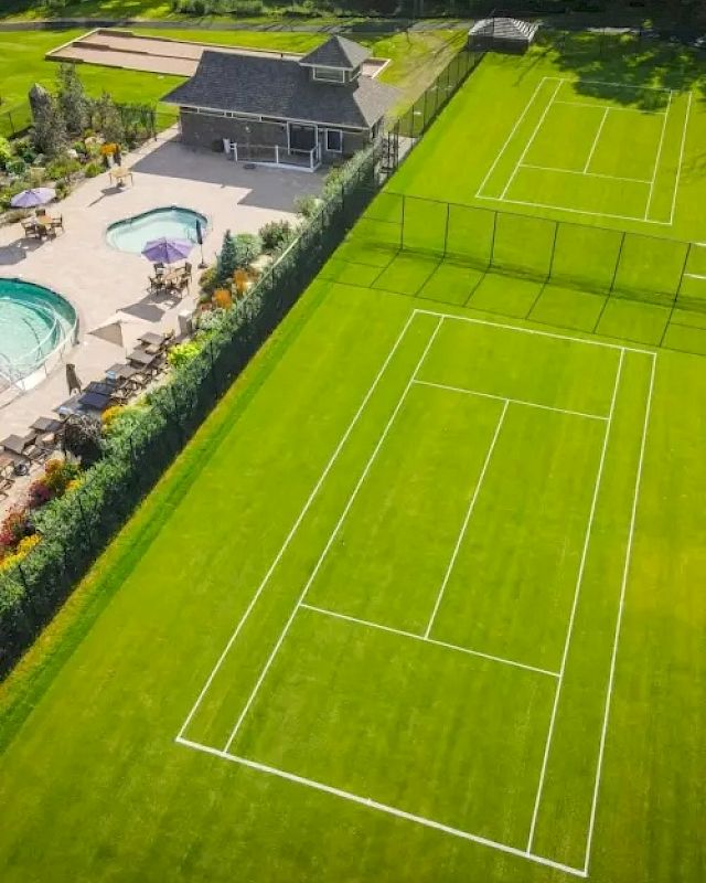 The image shows an aerial view of tennis courts and a swimming pool with lounge chairs, surrounded by greenery and a building.