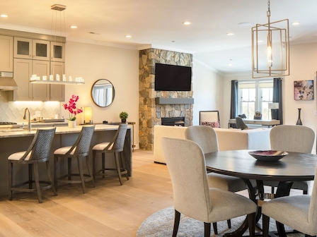 A modern open-concept living space with a kitchen, dining area, and seating area, featuring neutral decor and a stone fireplace.