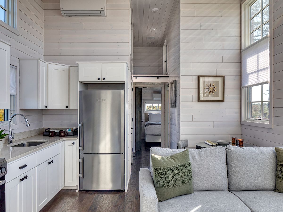 Bright kitchen and living area in a Tiny Home at The Preserve, featuring white cabinets, stainless steel appliances, and a cozy sofa.