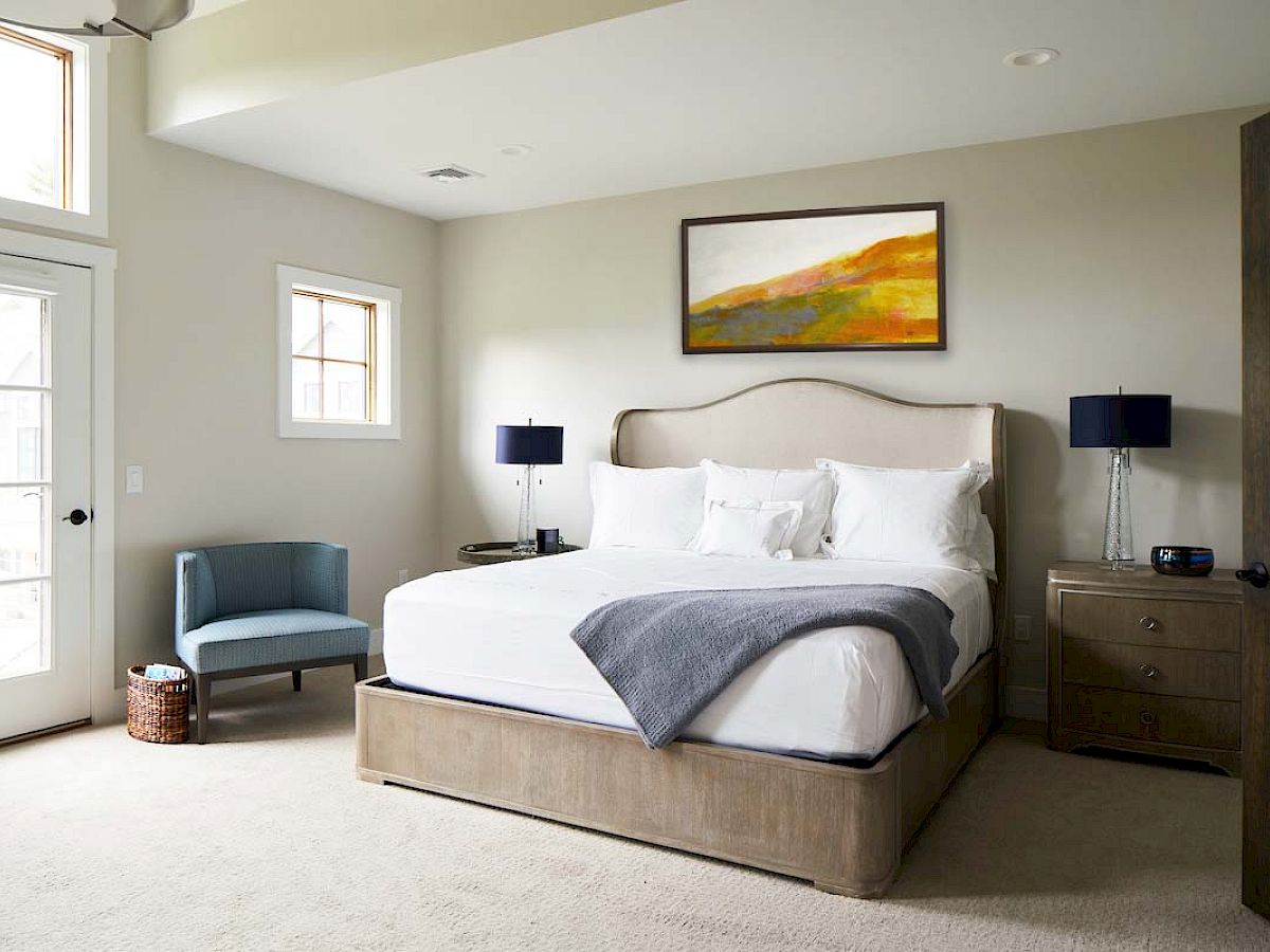 Elegant bedroom at the Hilltop Lodge, The Preserve, with a king-sized bed, soft lighting, and a scenic landscape painting above the headboard.