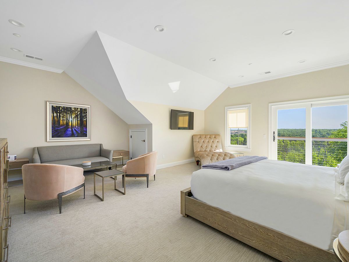 Luxurious bedroom at the Hilltop Lodge with a king-sized bed, sitting area, and balcony overlooking lush greenery.