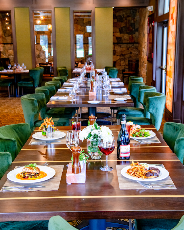 A beautifully set dining table in a restaurant with green velvet chairs, various meals and beverages, and elegant decor.