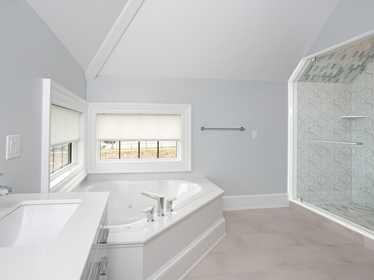 A modern bathroom with a bathtub, sink, and glass-enclosed shower. The walls are gray, and the space is well-lit by natural light.