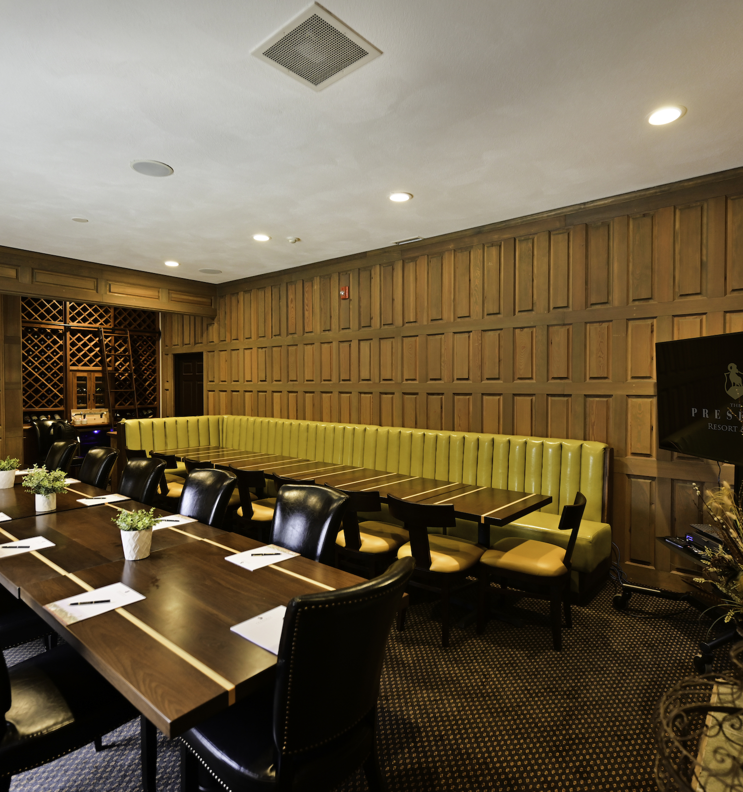 This image shows a well-furnished conference room with a long table, black chairs, and a yellow bench against the wood-paneled wall, ending the sentence.