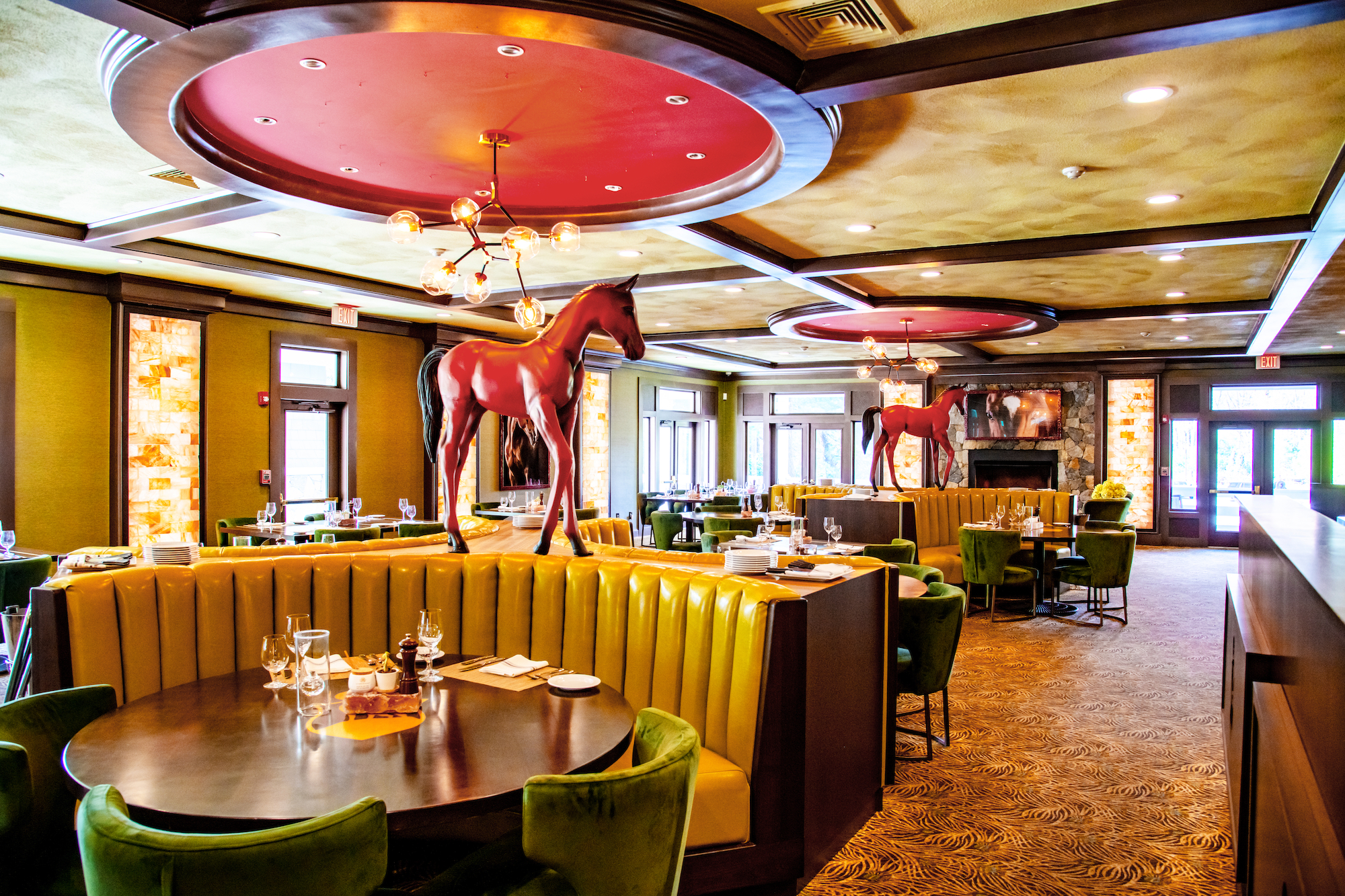 A stylish restaurant interior with green seating, round tables, and decorative horse statues in the center of the space.