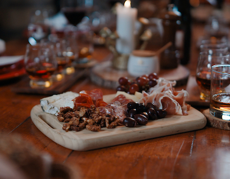 Charcuterie board with wine and whiskey glasses on a rustic wooden table.