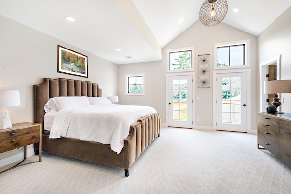 A spacious bedroom with a large bed, wooden nightstands, a dresser, and large windows allowing abundant natural light.