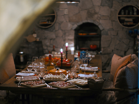 A cozy dining table set for a meal with candles, wine glasses, and various dishes. The stone wall and archway add to the warm ambiance.